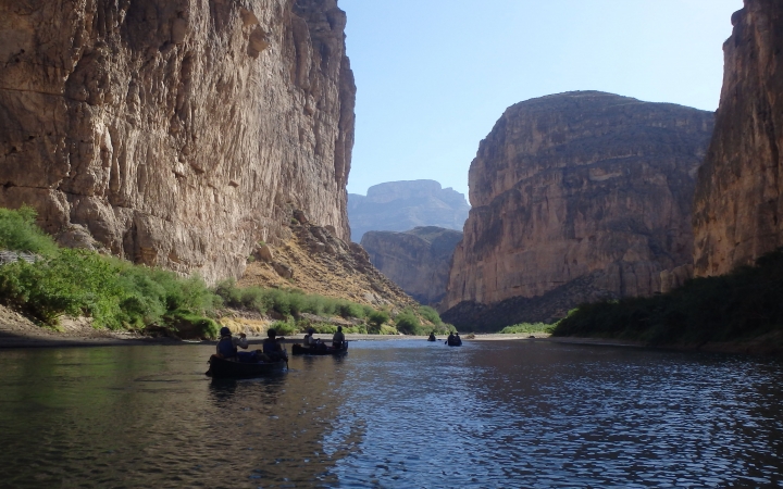a group of canoes are paddled along a river with high canyon walls on either side 